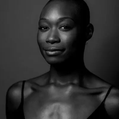 Black and white portrait photo of Nayaa Opong. They are smiling slyly looking into the camera, wearing a black top.