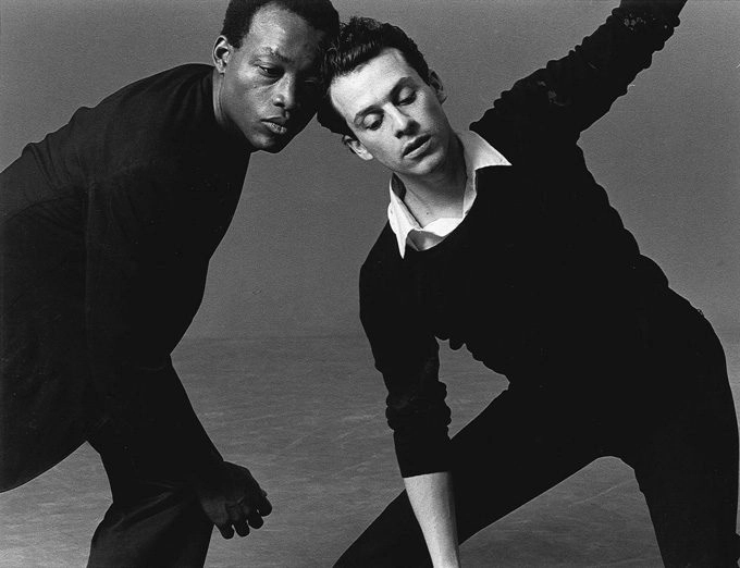Black and white photo of a young Arnie Zane and Bill T Jones posing in a studio wearing black outfits and swaying.
