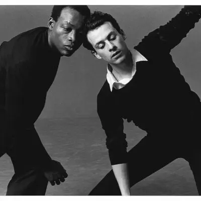 Archival black and white photo of Bill T Jones and Arnie Greenfield. They are in a dyanmic dance pose, with Arnie opening his body towards the camera.