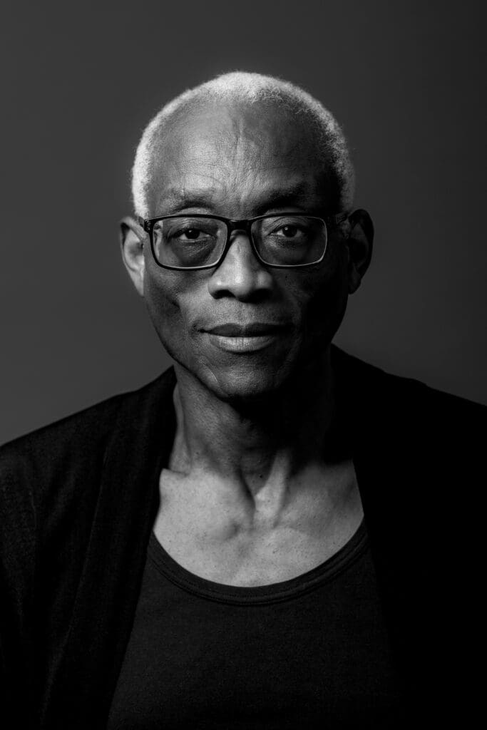 Black and white portrait of Bill T Jones wearing a black shirt and cardigan
