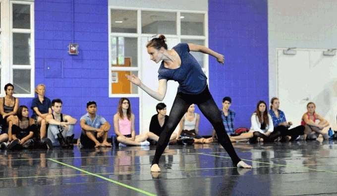 A woman dancing in front of studio class that is sitting around her.