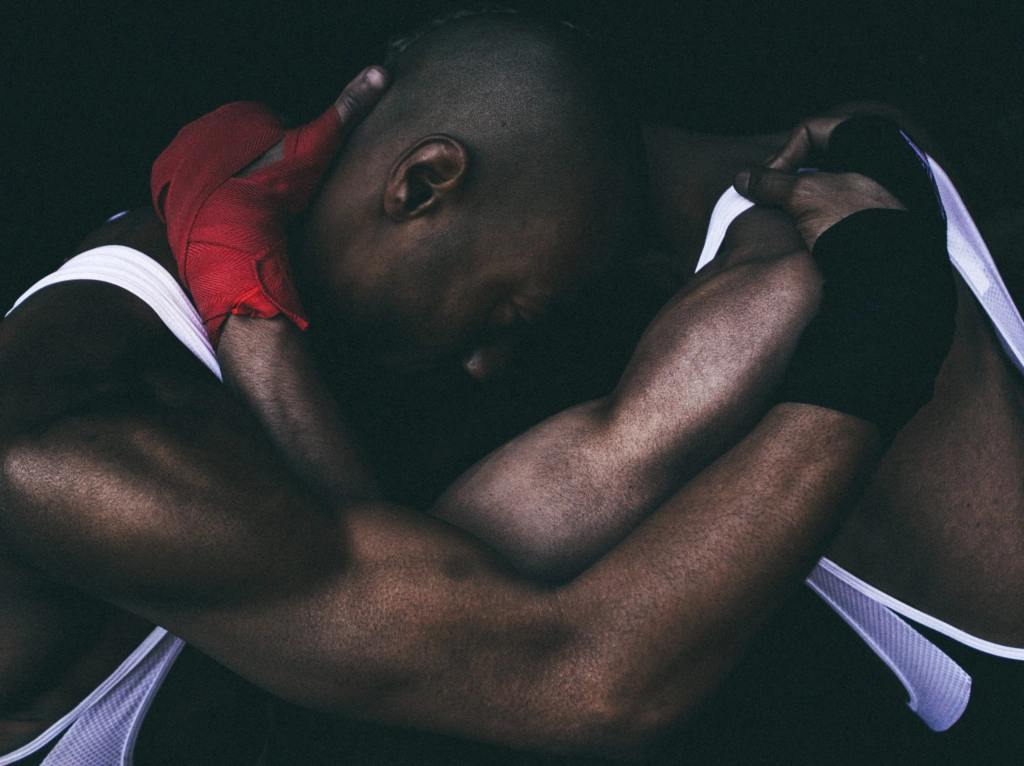 Dim side profile portrait of two figures locked in a position similiar to two boxers clutching each other