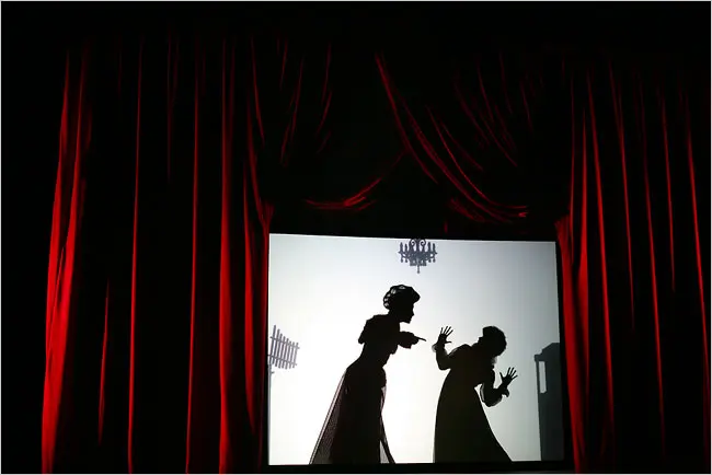 A silhouette of two people arguing is framed by red velvet curtains