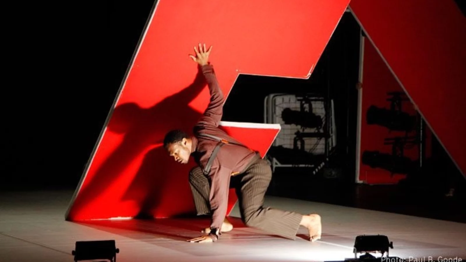 Dancer on a stage kneeling next to a giant red letter "E"