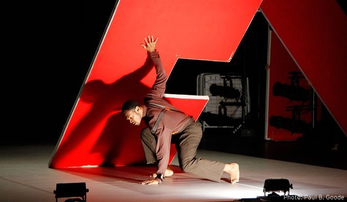 Dancer on a stage kneeling next to a giant red letter "E"