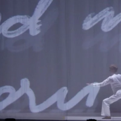 A dancer performs on a stage with huge images of handwriting projected behind them