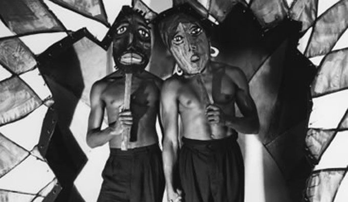Black and white photos of shirtless dancers holding large masks in front of their faces