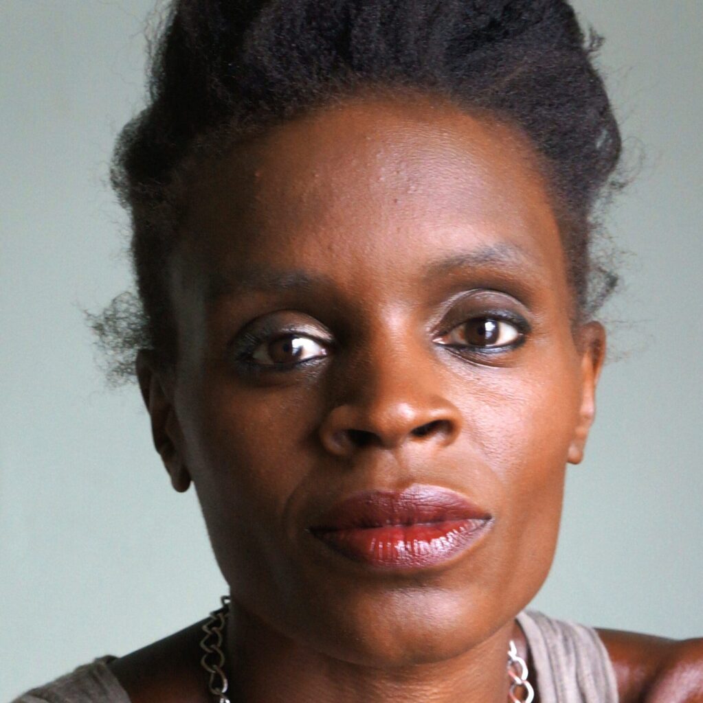 Color portrait photo of Okwui Okpokwasili. They face the camera against a grey background, wearing a grey tank top and silver necklace.
