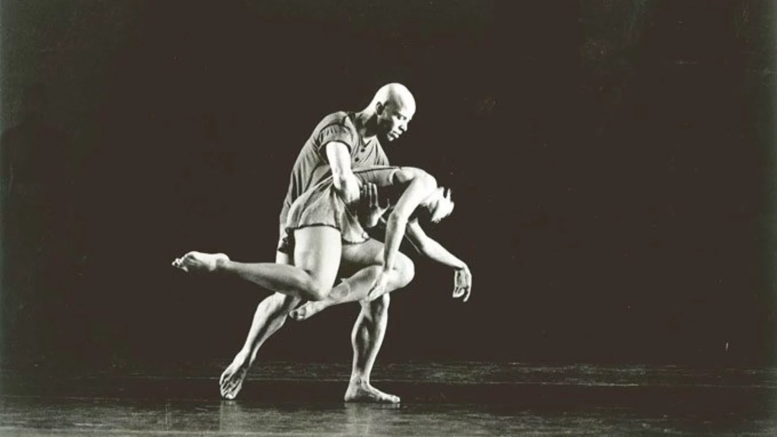 Black and white photo of a dancer, who is carrying the frail limp body of another