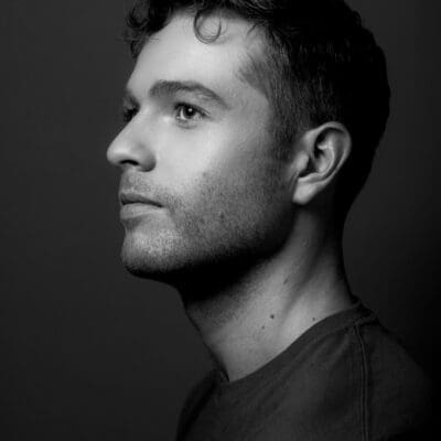 Black and white side profile portrait photograph of Shane Larson. They are looking off to the upper left of the image, wearing a black t shirt.