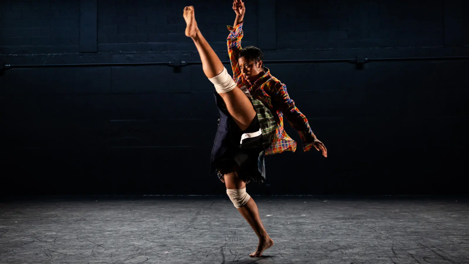 A black femme with a curly mullet dances through space in overlaying patterned clothes